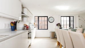 Una cocina moderna con armarios blancos, un reloj y un comedor con sillas.