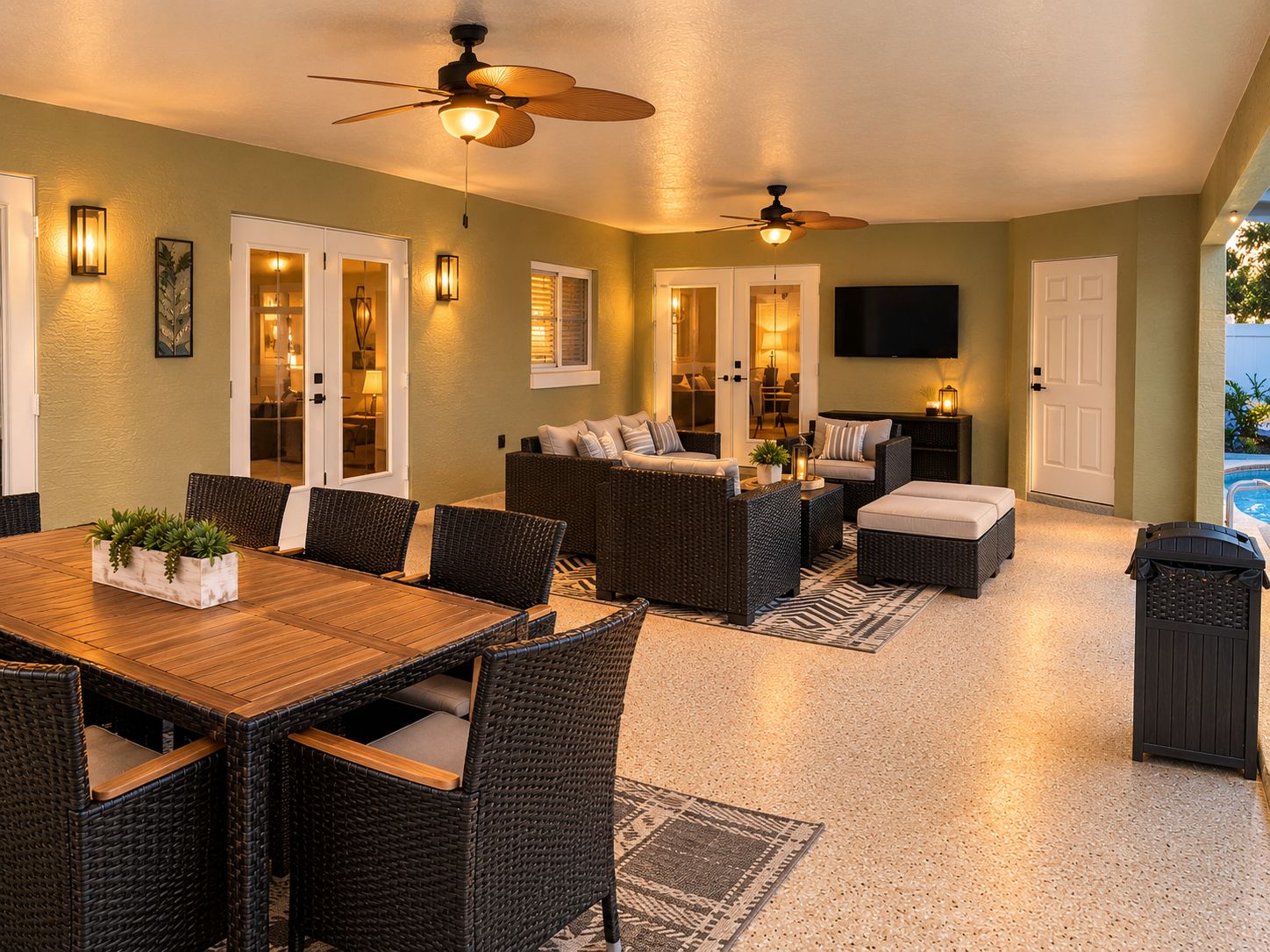 A spacious indoor area with a dining table, wicker furniture, ceiling fans, and a TV mounted on the wall.