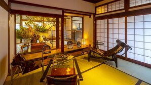 A traditional Japanese room with tatami flooring, a low table with a cushion, a wooden chair, and a sliding door with a view of greenery outside. - Shisekiryokan Kagetsu Taisyokan (Takeo)