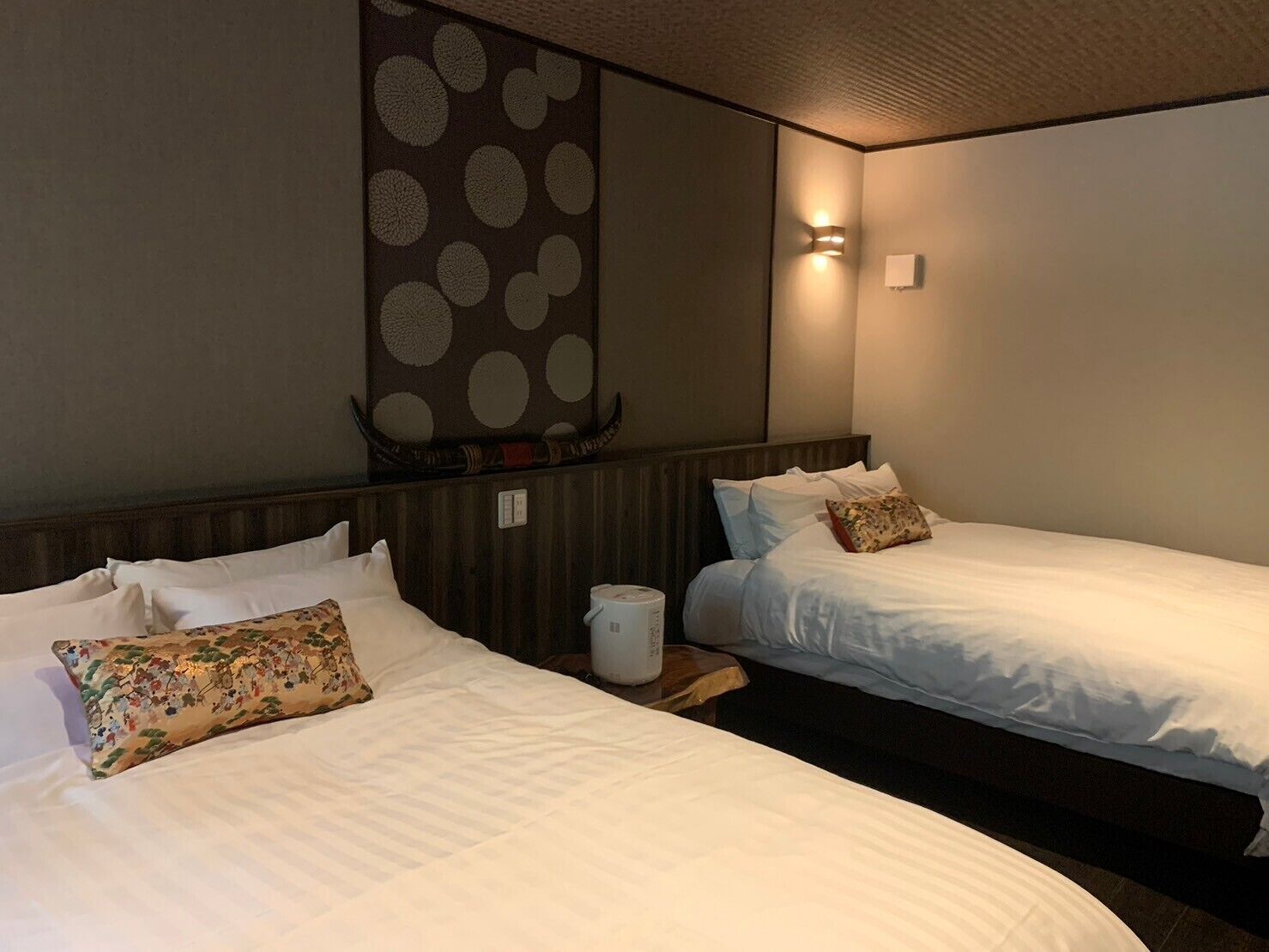 A hotel room with two beds, a wall-mounted heater, and a wall decoration.