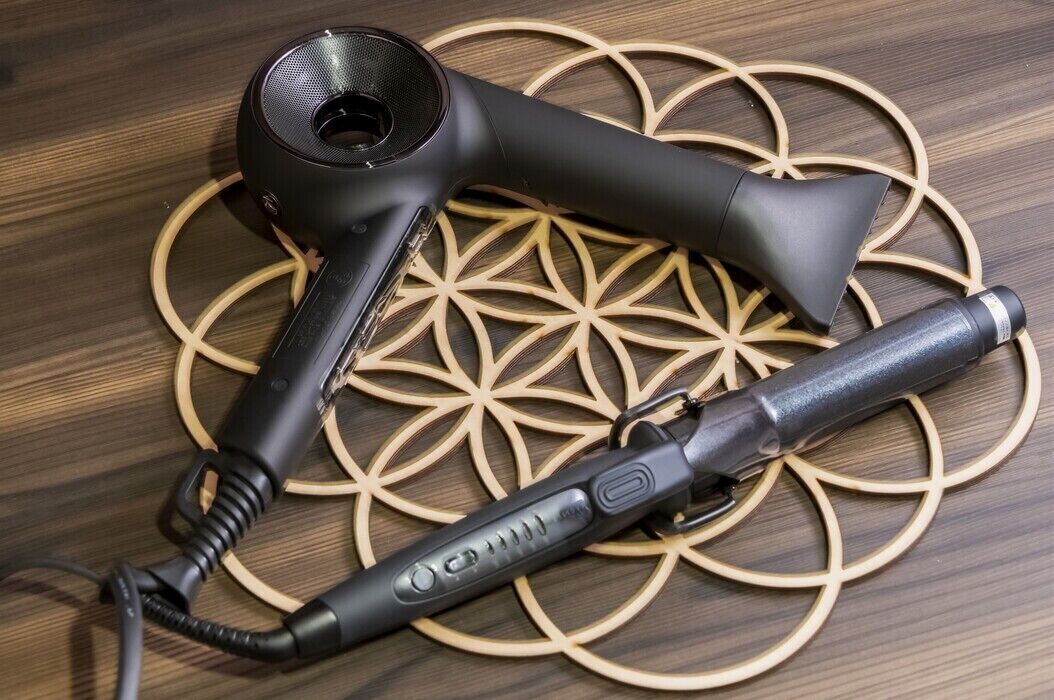 A hair dryer and a curling iron on a wooden surface with a geometric pattern.