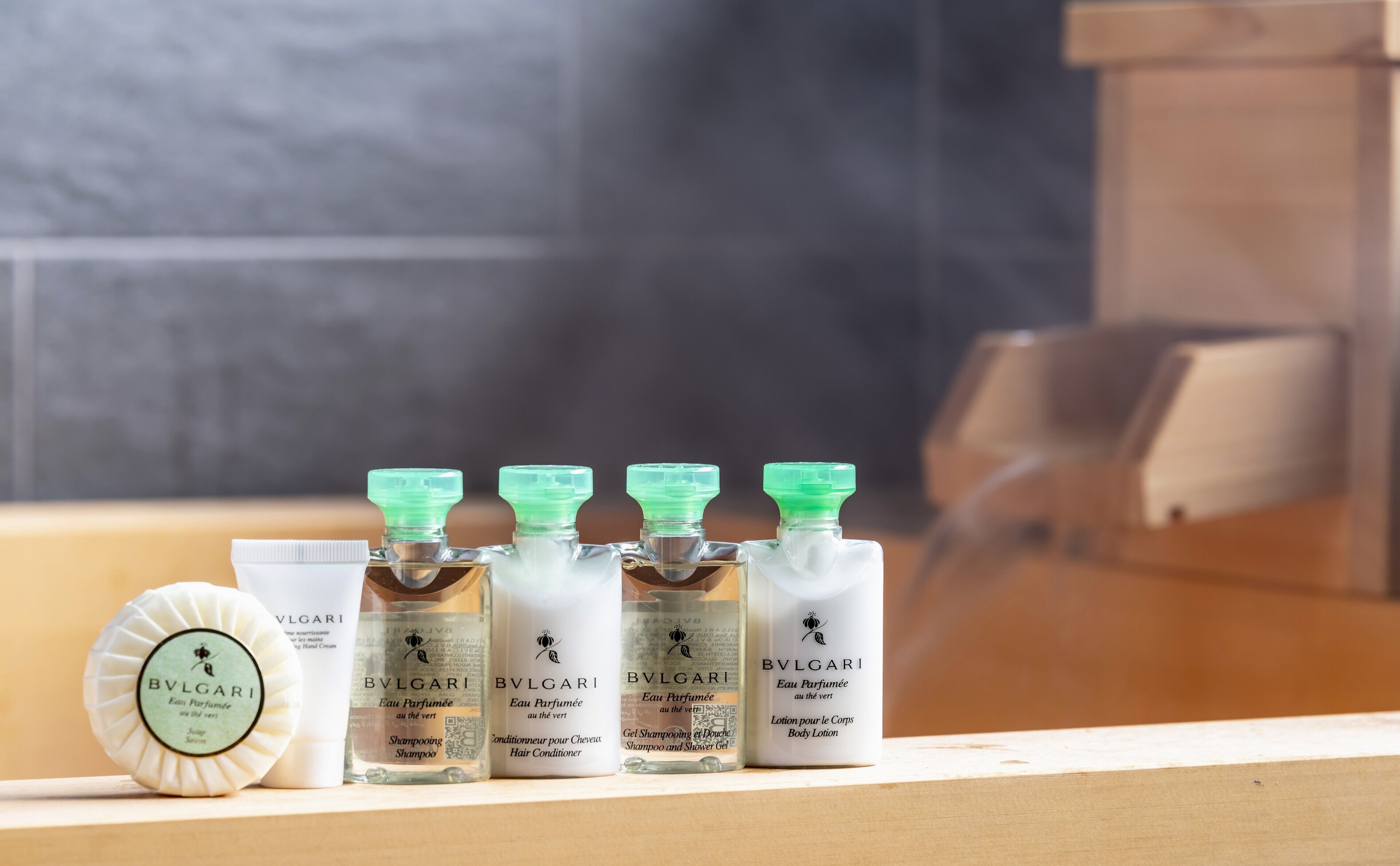 A row of luxury skincare products, including hand cream, shampoo, and body lotion, displayed on a wooden shelf.
