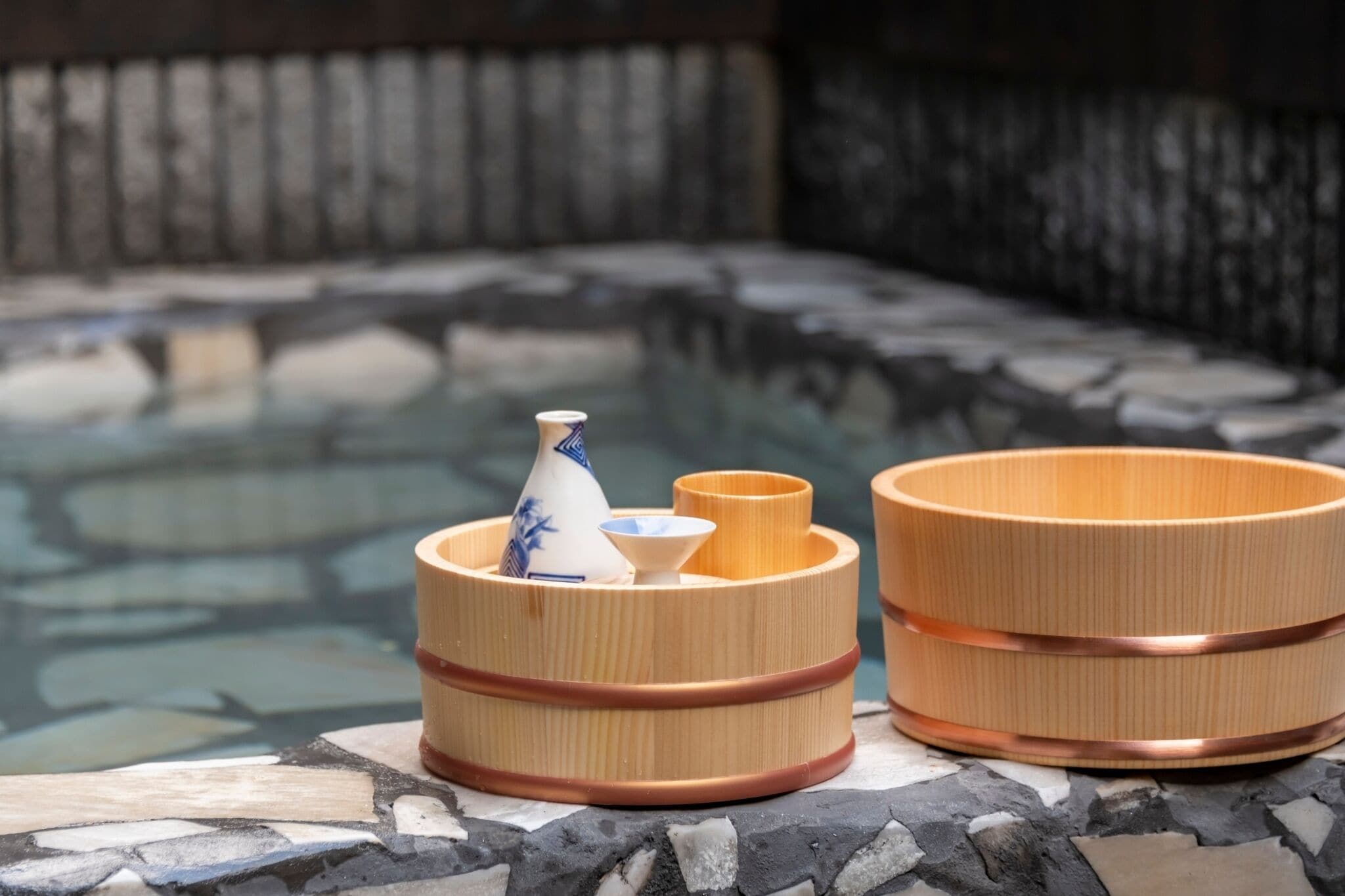 A hot spring area with stone flooring and a wooden structure containing a vase and bowls.