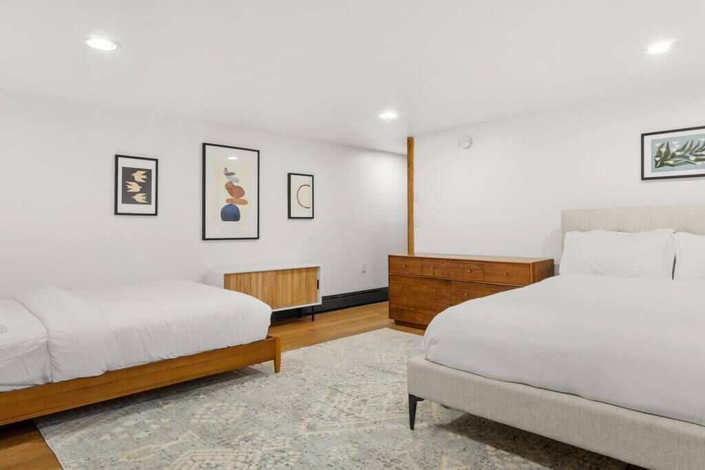 Ein modernes Schlafzimmer mit zwei Betten, einer Holzkommode und einem großen Teppich.