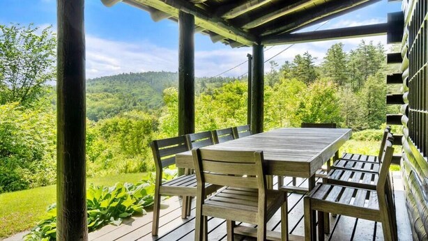 Een houten terras met tafel en stoelen, met uitzicht op een weelderig groen landschap.
