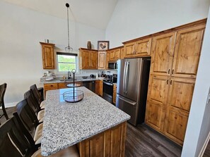 A kitchen with granite countertops, wooden cabinets, a stainless steel refrigerator, and a hanging light fixture. - Mtn Paradise Lake View Heated Indoor Pool Splashpad (Branson)
