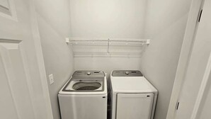 A compact laundry room with two front-loading washing machines and a metal shelf above them. - Mtn Paradise Lake view Indoor/Outdoor pools/2 splash pads, Silver Dollar City (Branson)
