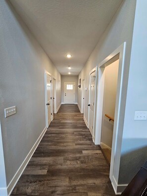A hallway with wooden flooring, white walls, and doors leading to rooms.