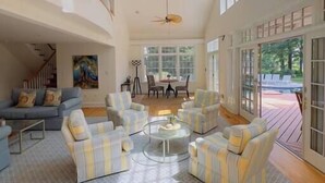 A spacious living room with a high ceiling, a staircase, and large windows. - St. Michaels Escape | Pool, Hot Tub & Fire Pit (Saint Michaels)