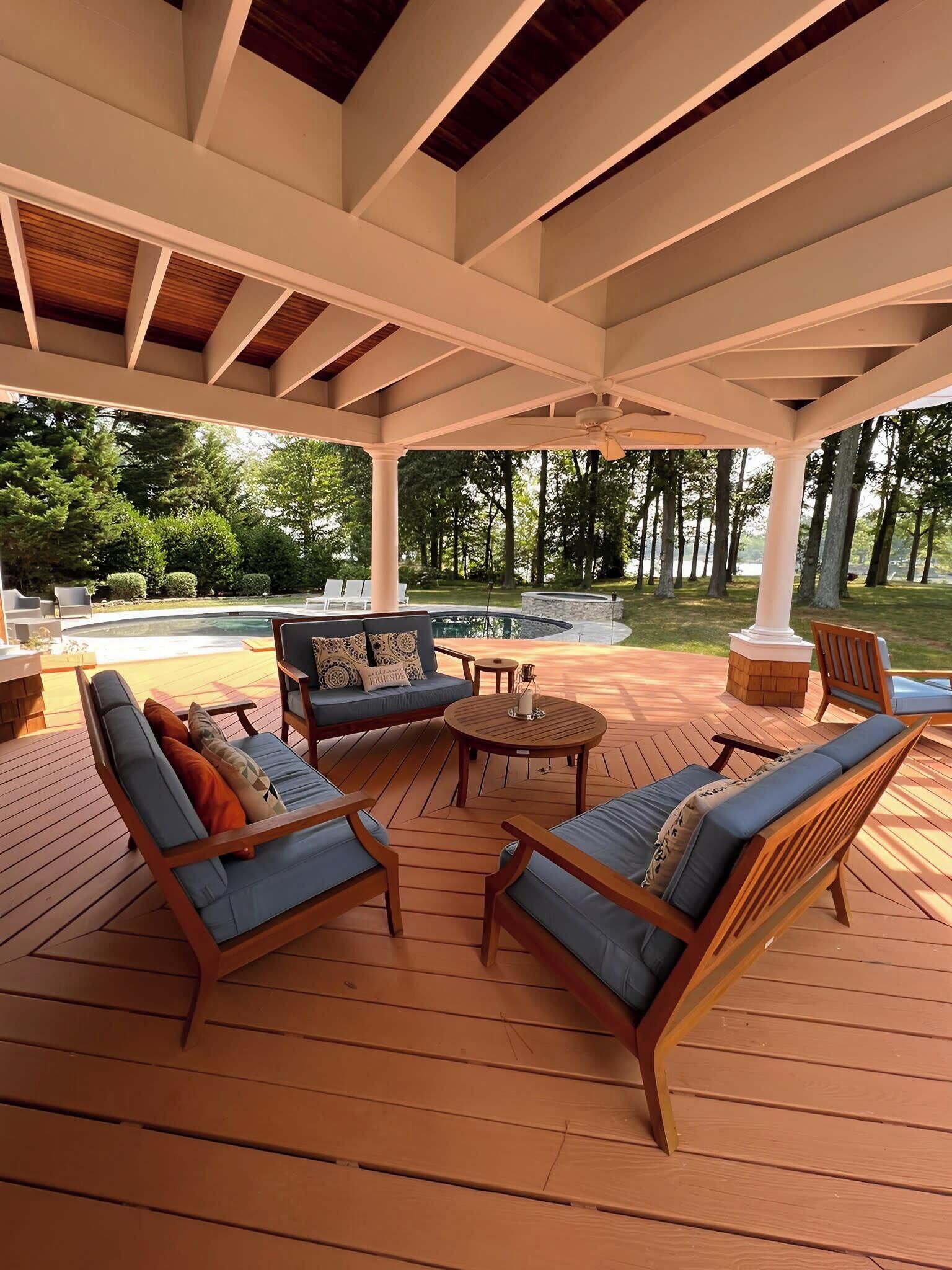 A covered outdoor seating area with wooden furniture and a view of a swimming pool.