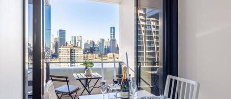 A balcony with a table set for two, overlooking a cityscape.