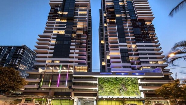 A high-rise building with multiple balconies and a green wall at the base.