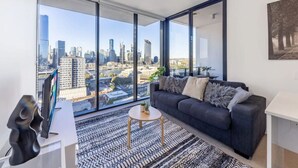 A modern living room with a large window, a sofa, a coffee table, and a TV.
