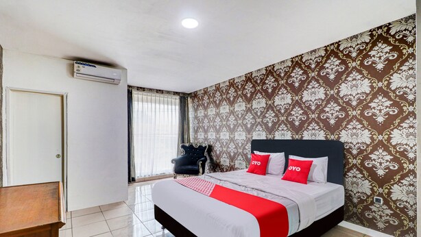 A hotel room with a bed, a chair, a desk, and a window with curtains.
