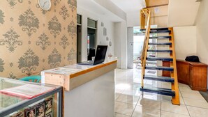 A reception desk with a laptop, a clock, and a patterned wallpaper. A wooden staircase is visible in the background.