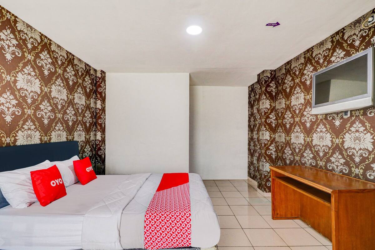 Habitación de hotel con cama, televisor en la pared y papel tapiz estampado.