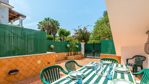 An outdoor dining area with a green and white striped tablecloth, green chairs, and a tiled patio. - Friendly Family Apartment at Ischia (Ischia)