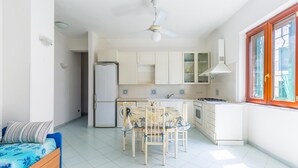 A compact kitchen with white cabinets, a built-in oven, and a dining table with chairs. - Friendly Family Apartment at Ischia (Ischia)