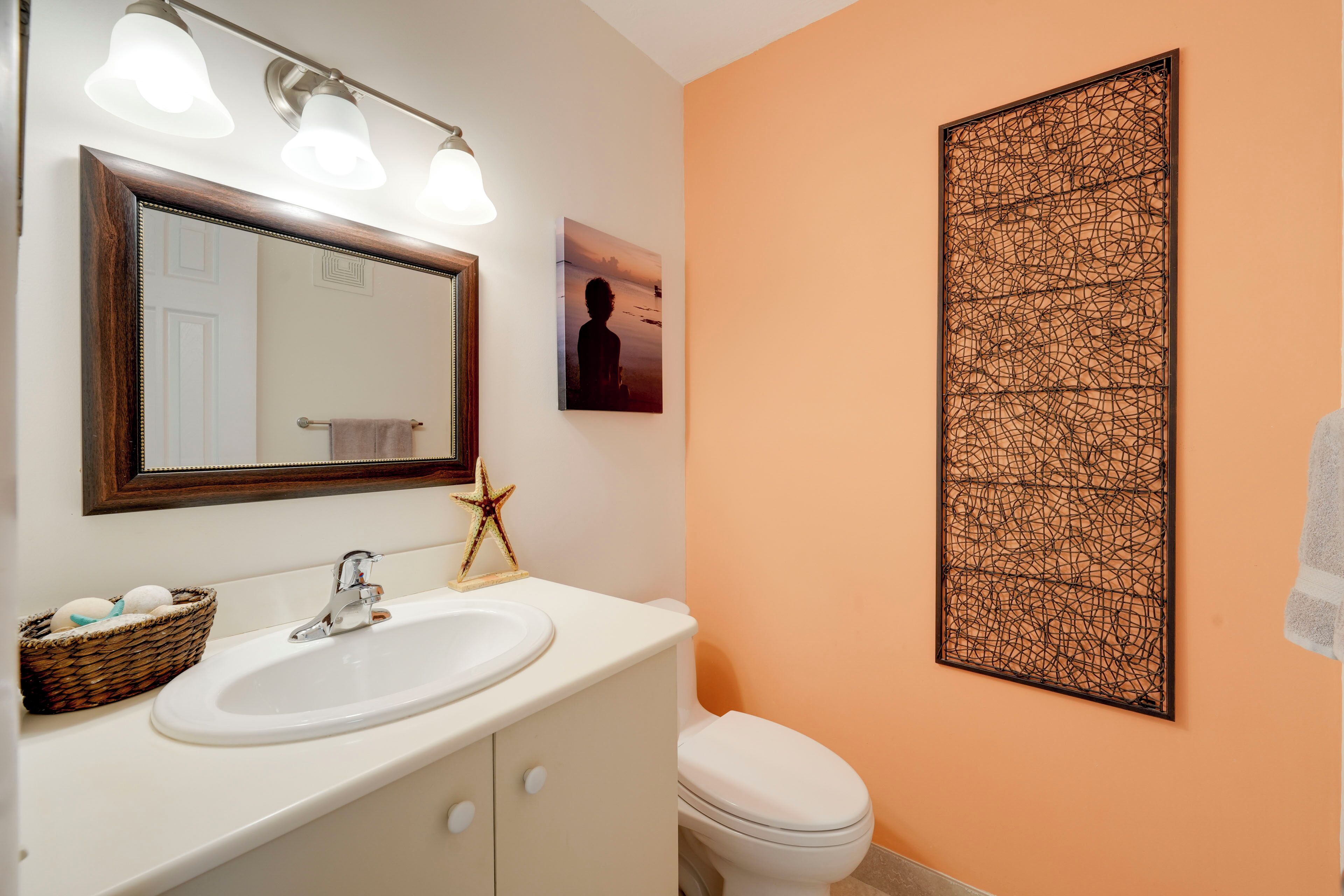 Een badkamer met een witte wastafel, een spiegel en een toilet. Op de wastafelrand ligt een decoratieve ster en een mand met eieren.