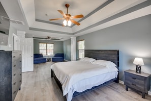 A bedroom with a large bed, a ceiling fan, a nightstand with a lamp, and a dresser.