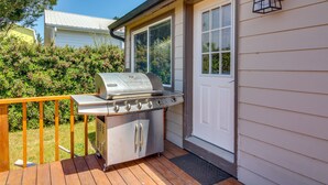 Ein Grill auf einer Holzterrasse, eine weiße Tür und ein Fenster mit Blick auf Grünflächen.