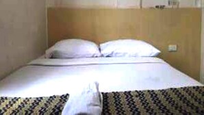 Una habitación de hotel con una cama, cabecera y una mesita de noche con lámpara.