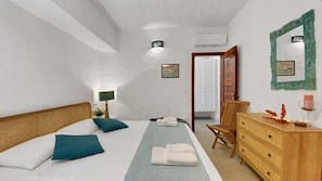 A bedroom with a bed, a dresser, a chair, a bedside table with a lamp, a mirror, and a picture on the wall.