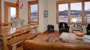 Een gezellige woonkamer met een houten tafel, een leren bank en uitzicht op een besneeerd landschap door grote ramen.