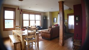 Een ruime woonkamer met een houten eettafel, stoelen, een bank en een groot raam dat natuurlijk licht binnenlaat.