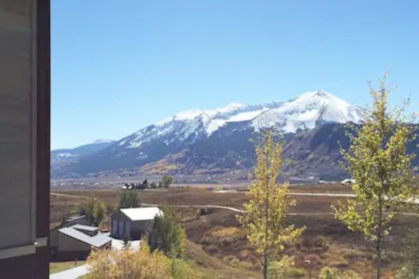 Une vue sur une montagne dont le sommet est enneigé, un ciel dégagé et quelques bâtiments au premier plan.