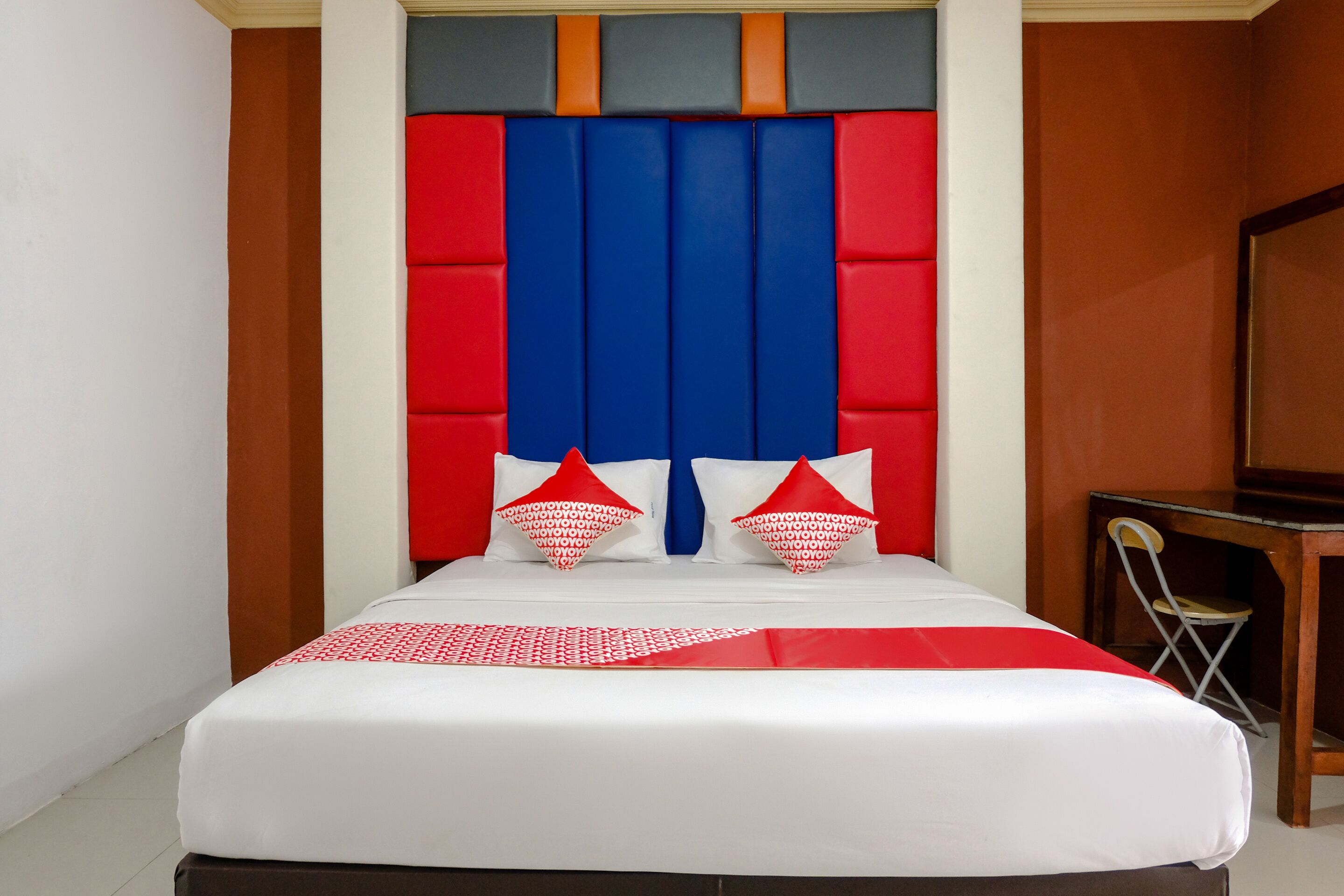 Una cama con una colcha blanca y roja, dos almohadas rojas y un cabecero azul.