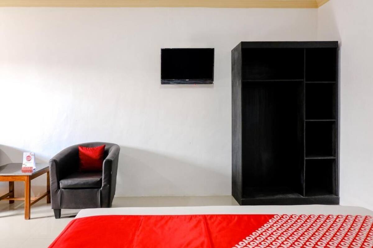 Een kamer met een bed, een zwarte stoel met een rode kussen, een kleine tafel, een zwarte kast en een tv aan de muur.