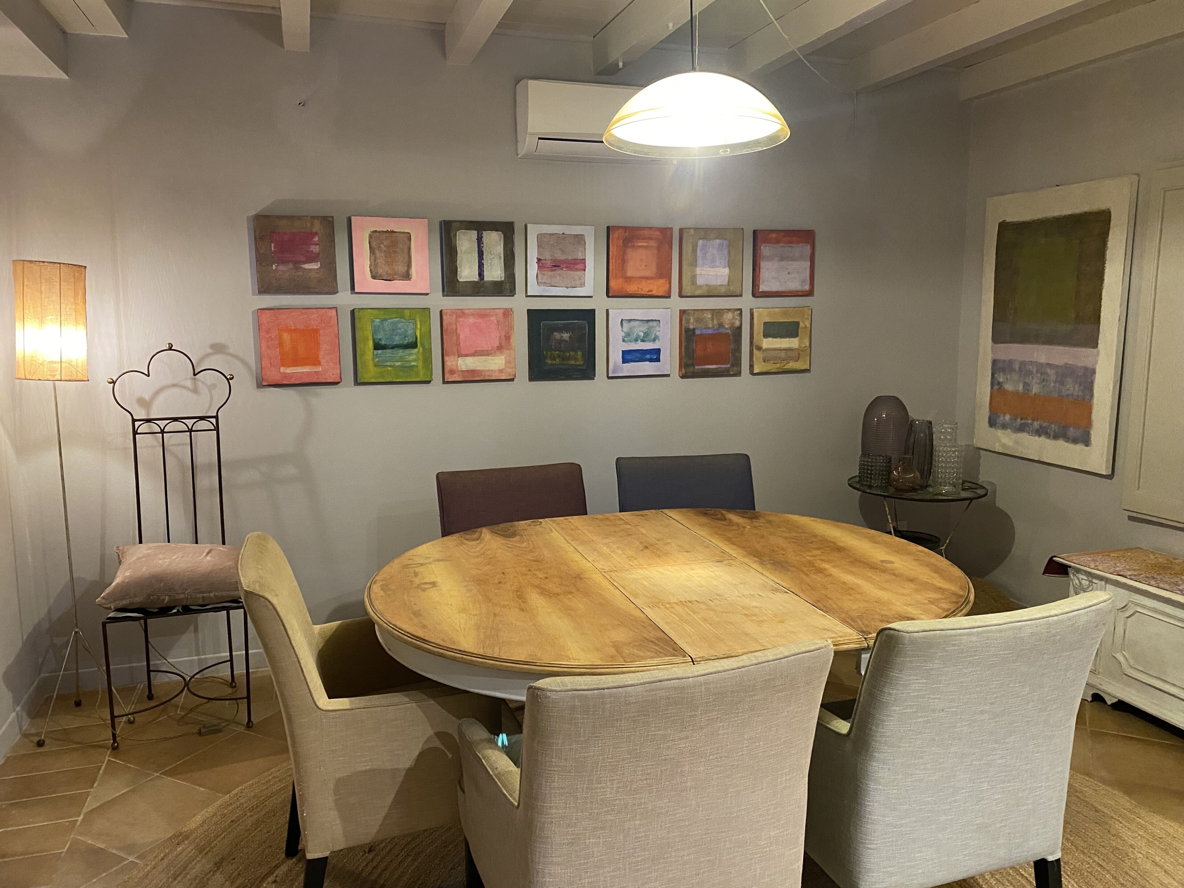 Un comedor con una mesa redonda de madera, seis sillas y una pared decorada con cuadros.