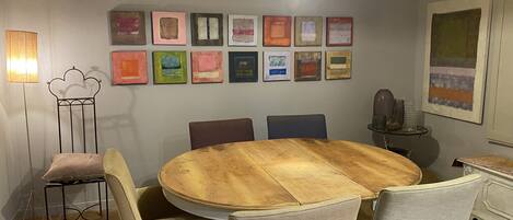 Un comedor con una mesa redonda de madera, seis sillas y una pared decorada con cuadros.