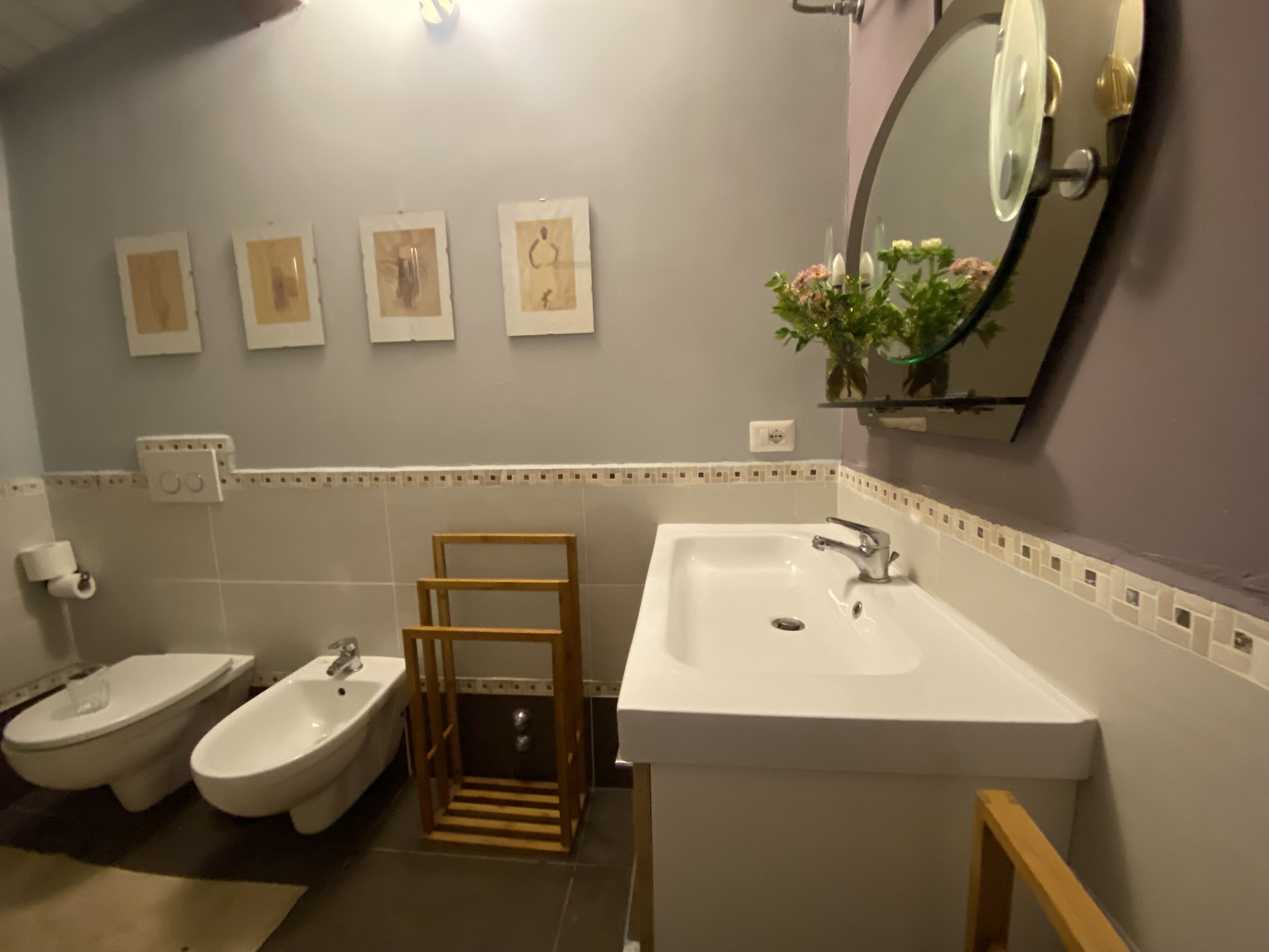 Un bagno con due servizi igienici, un lavandino e uno specchio. Sulle pareti, quattro quadri con cornice.