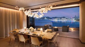 Comedor con una gran mesa dispuesta para seis personas, un candelabro y vistas a la ciudad a través de amplias ventanas.