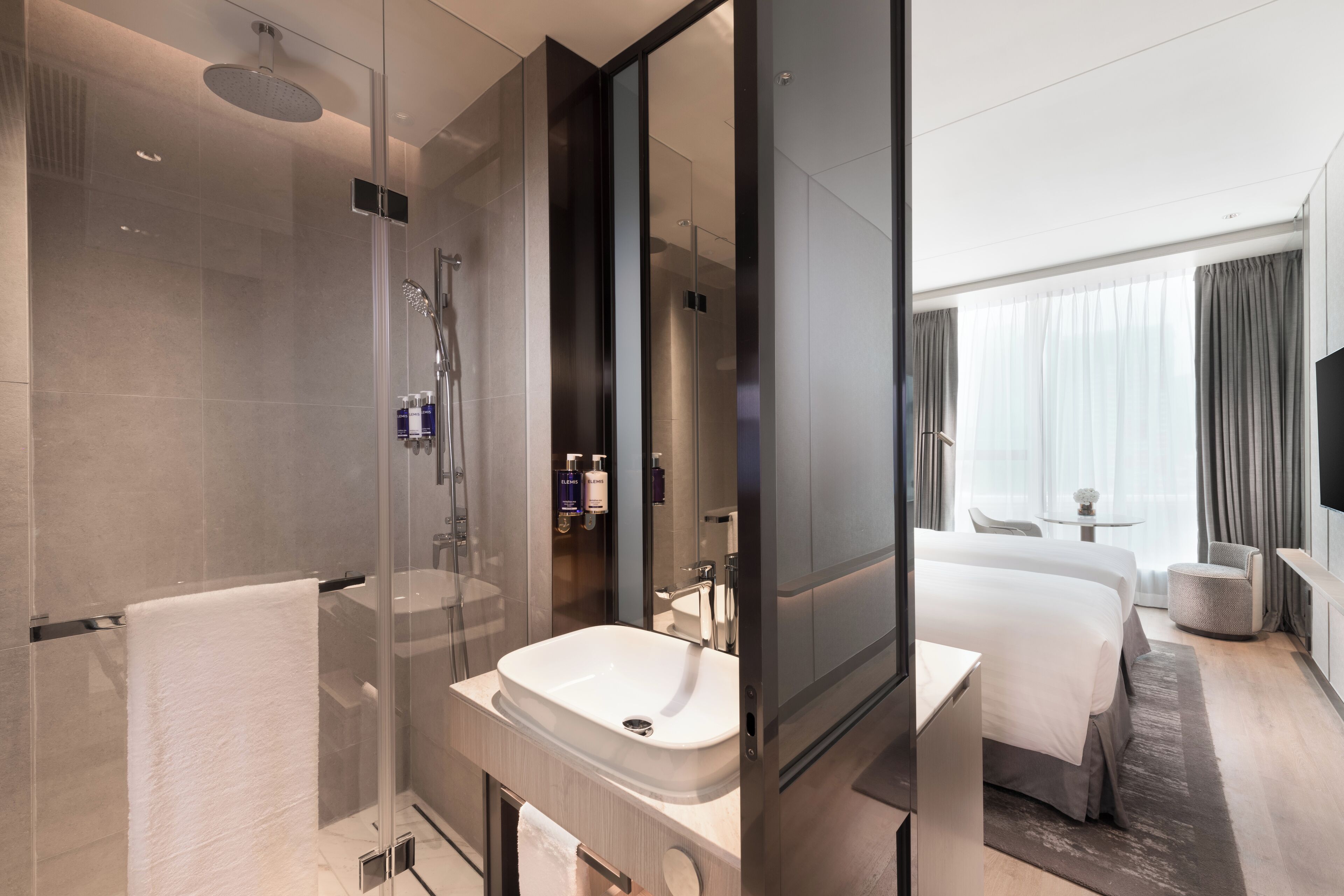A modern hotel bathroom with a glass-enclosed shower, a large sink, and a visible mirror.