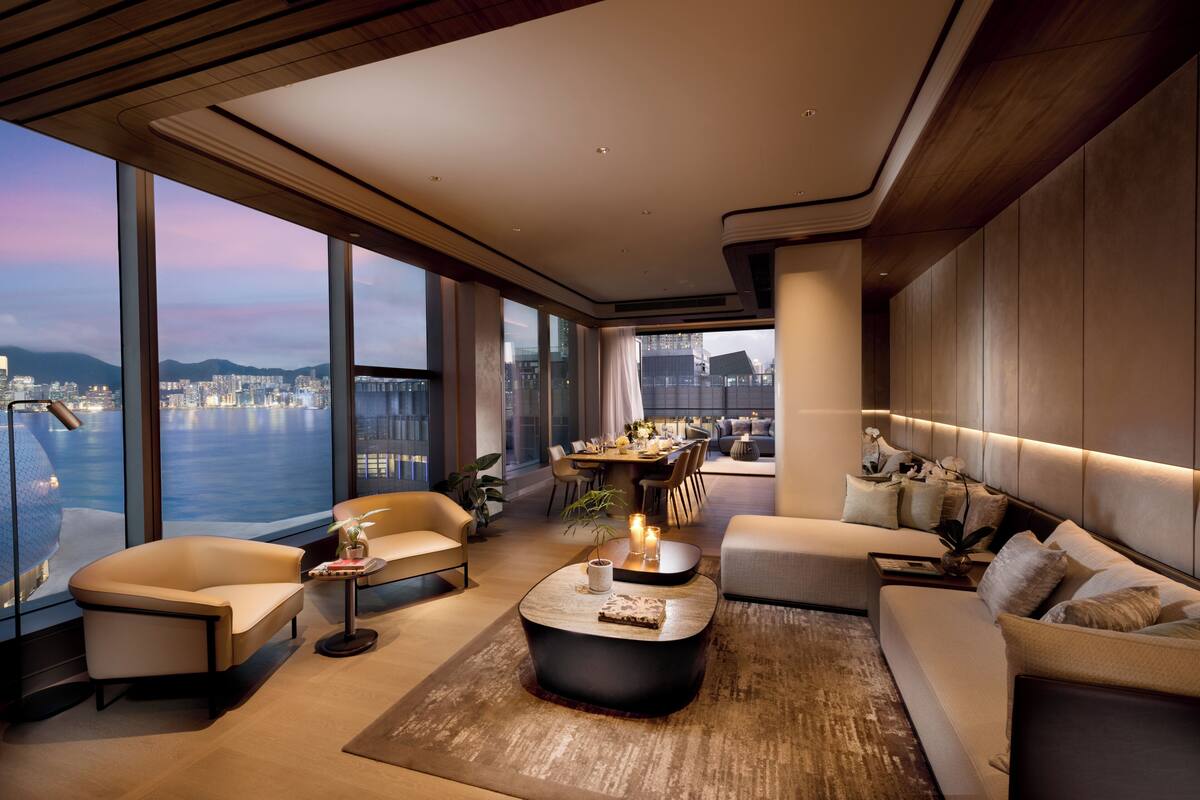 A modern living room with a large window overlooking a cityscape and water. There is a sofa, a coffee table, and a dining area with a table and chairs.