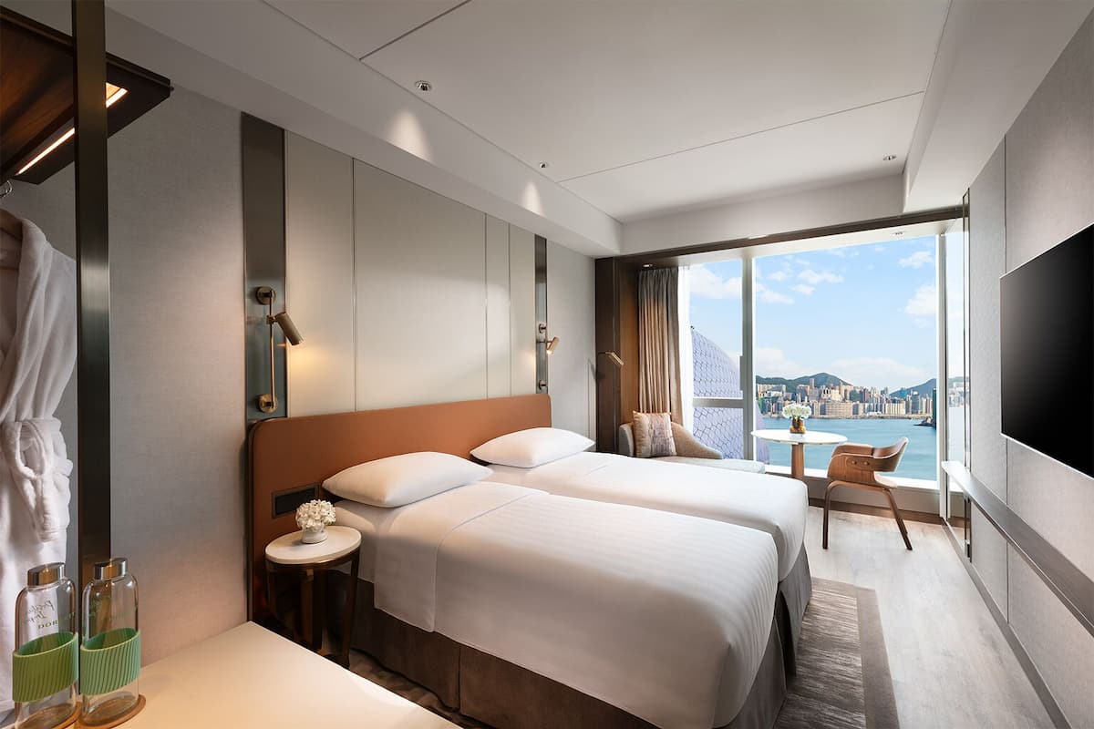 A hotel room with two beds, a TV, a view of the city, and a balcony with a table and chair.