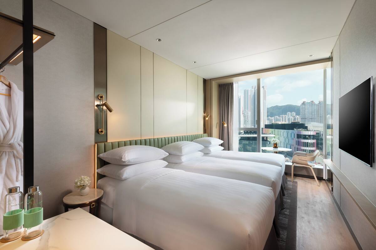 A hotel room with two beds, a TV, a small table with a chair, and a view of the city.