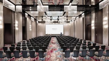 Un salón de conferencias con filas de sillas, una pantalla grande y una alfombra estampada con motivos florales.