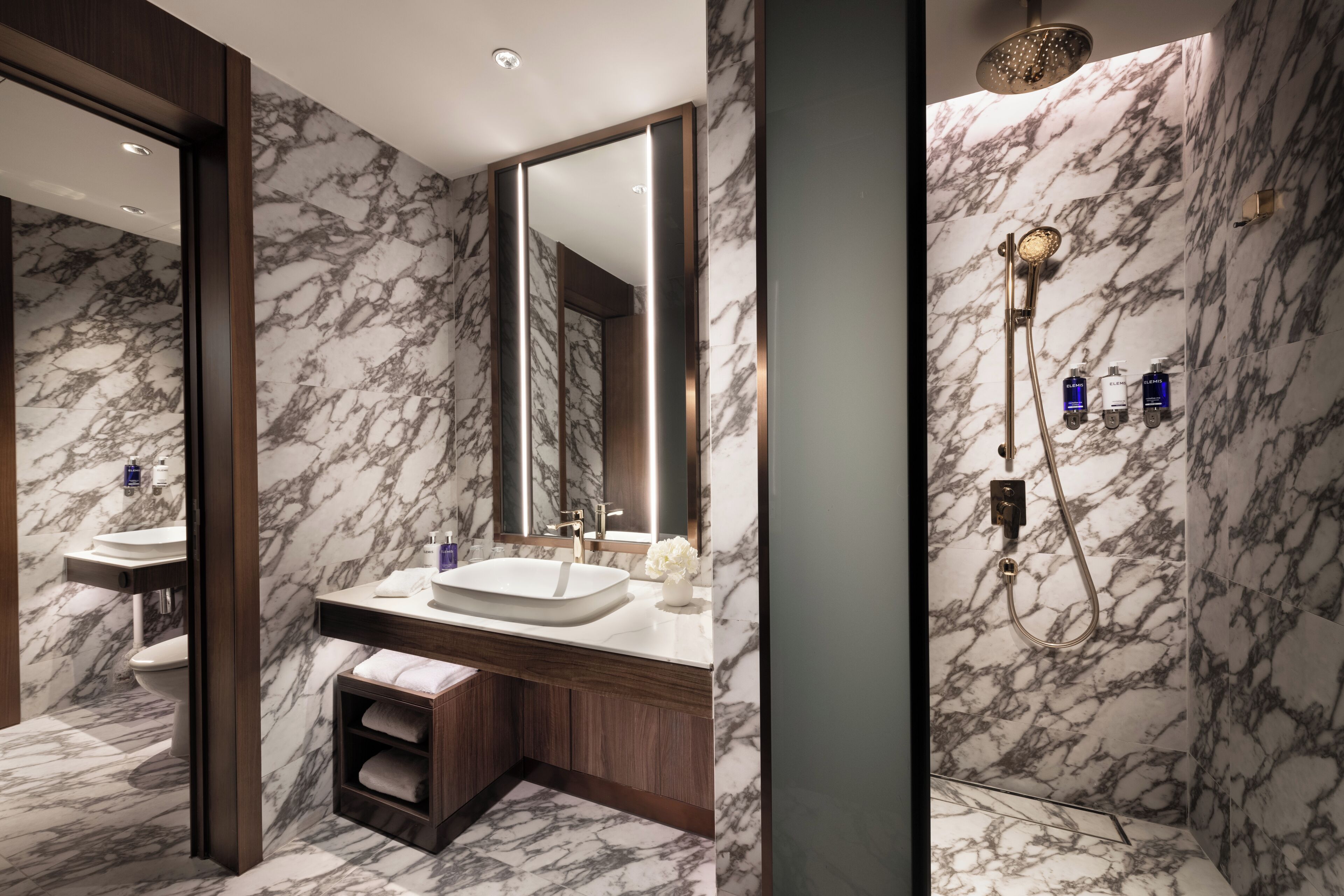 A modern bathroom with marble walls, a large mirror, a sink, and a shower area.