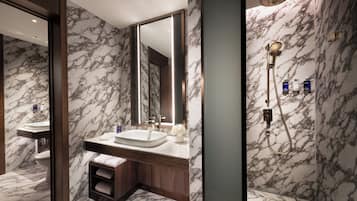 A modern bathroom with marble walls, a large mirror, a sink, and a shower area.