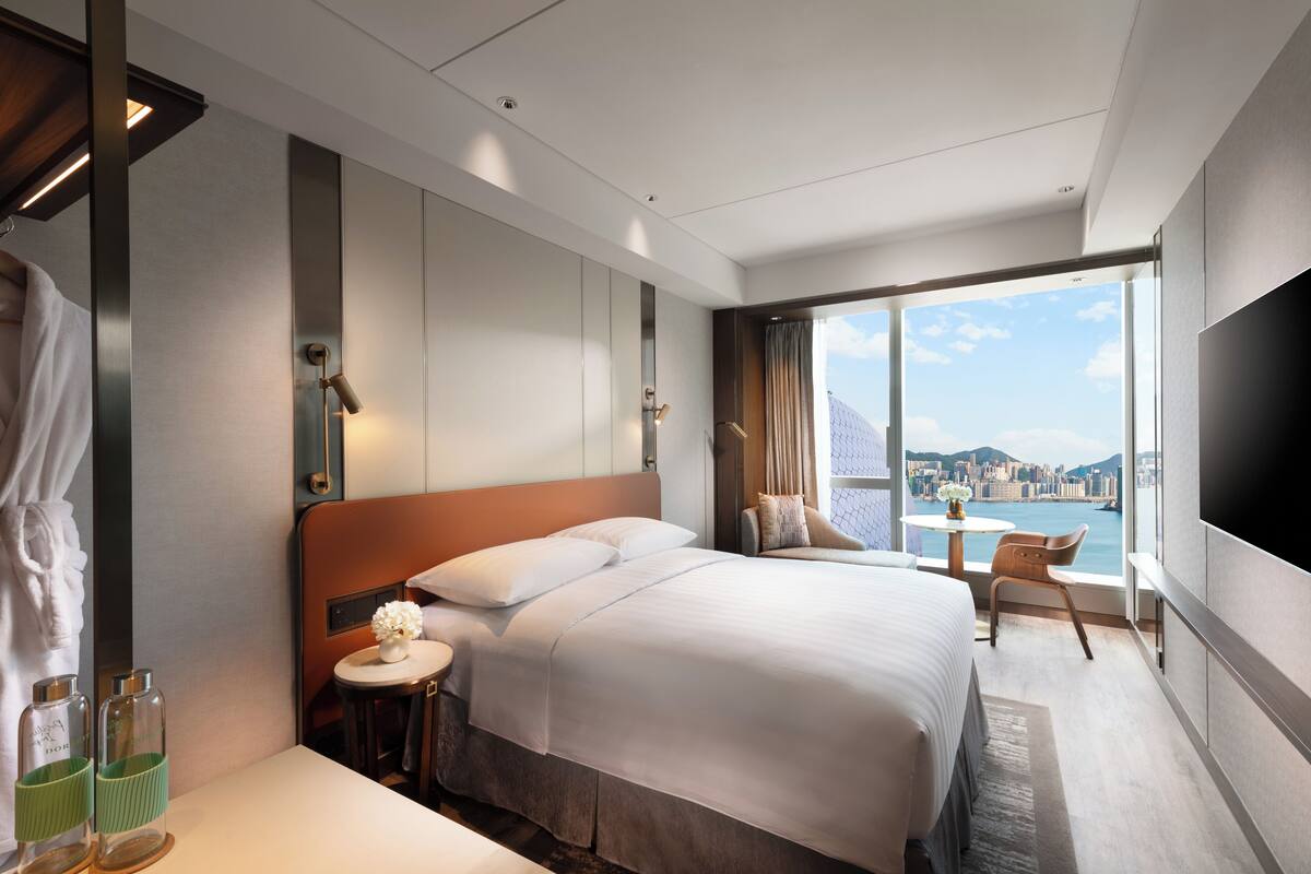 A modern hotel room with a large bed, a small table with a vase, a chair, and a TV.