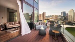 Un balcón moderno con un sofá, sillas y una mesita, con vistas a un paisaje urbano con edificios altos.