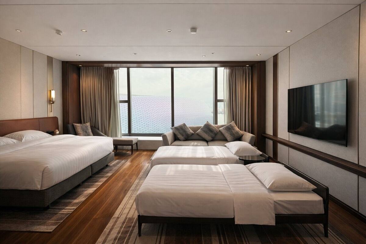 A hotel room with two beds, a sofa, a TV, and a large window with curtains.