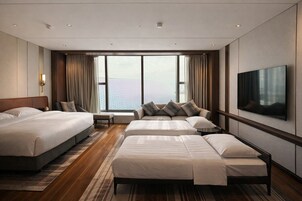 Habitación de hotel con dos camas, un sofá, un televisor y un ventanal con cortinas.