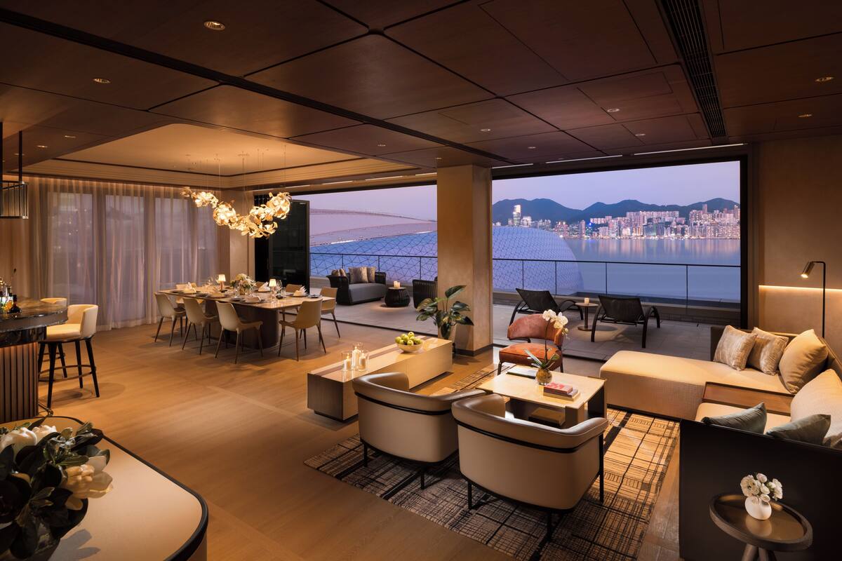A spacious living area with a dining setup, comfortable seating, and a large window offering a city and water view.