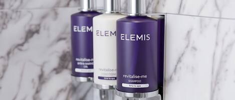 Three ELEMENTIS shampoo bottles mounted on a wall with a marble background.