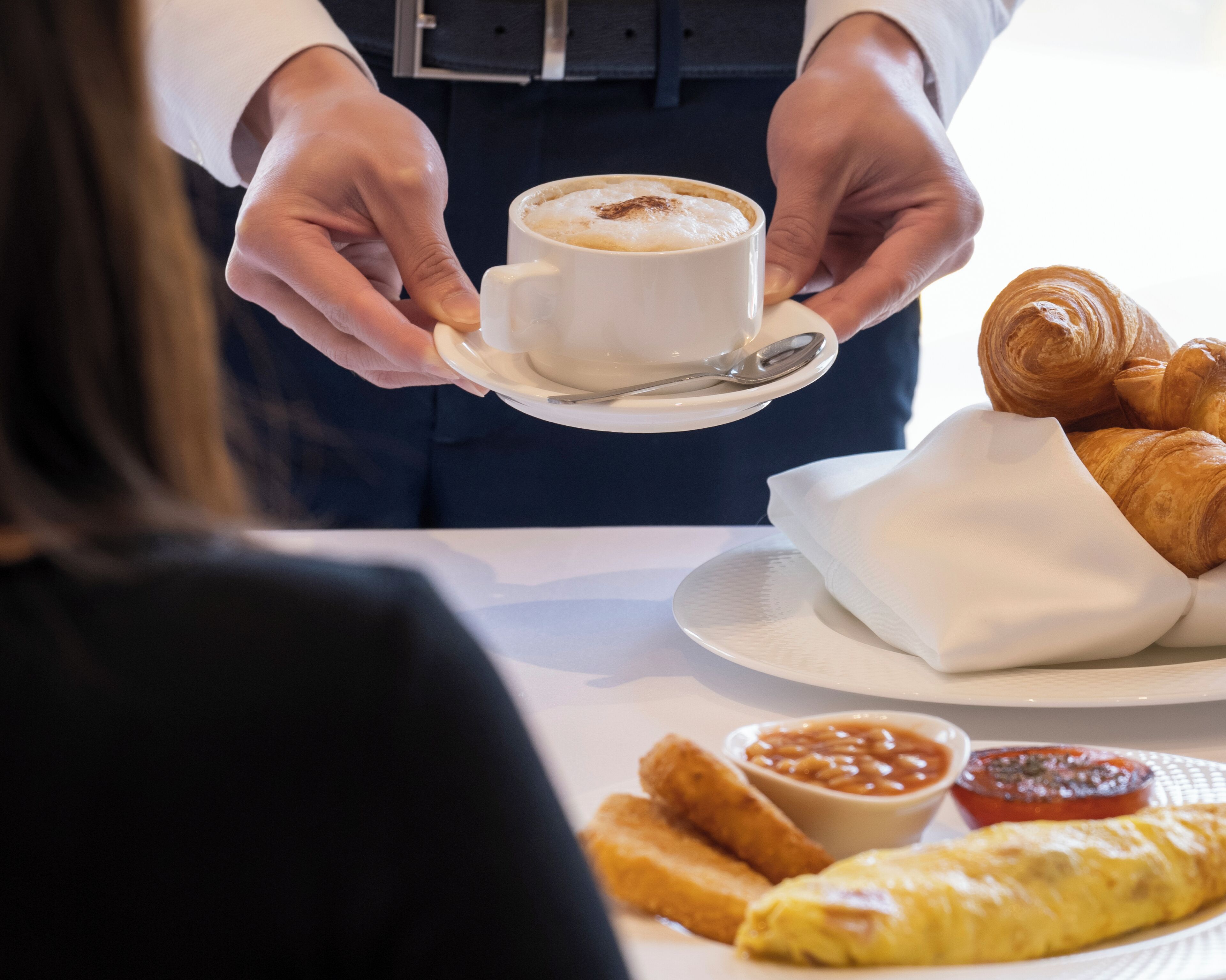 A waiter holding a cup of coffee and a plate with croissants and food items.
